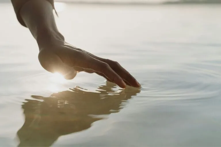 Hand die rustig het wateroppervlak raakt, symbool voor nazorg na een overlijden